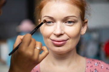 Professional female makeup artist applying cosmetics on pregnant woman face use brush working at beauty salon