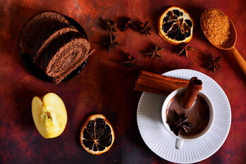 winter warm drink. Cup of hot liquid cocoa chocolate with cinnamon and star anise. Top view on table decorated with spices and herbs, apple slice, dry lemon, chocolate roll and spoon of brown sugar