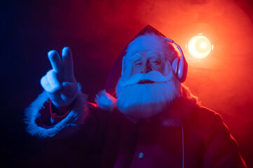Santa claus listens to music with headphones at a party. Blue red neon light and smoke.