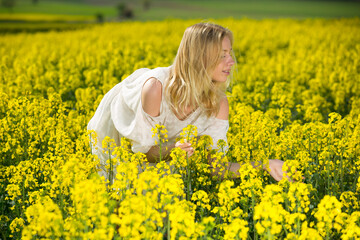 Fototapeta premium Happy girl posing in rape seed flowers field posing in white dress at sunny day outdoor