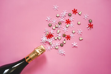 Christmas and New Year flatlay. Champagne bottle, wood star and snowflakes confetti on pink background top view. Flat lay holiday card. Birthday or party concept. Festive decorations