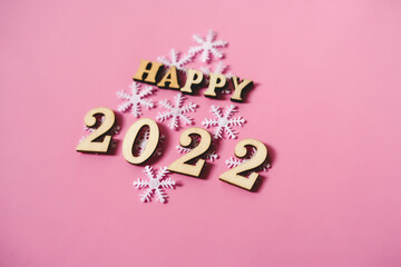 Happy New Year 2022. Quote made from wooden letters and numbers 2022 on pink background decorated snowflakes