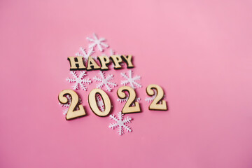 Happy New Year 2022. Quote made from wooden letters and numbers 2022 on pink background decorated snowflakes