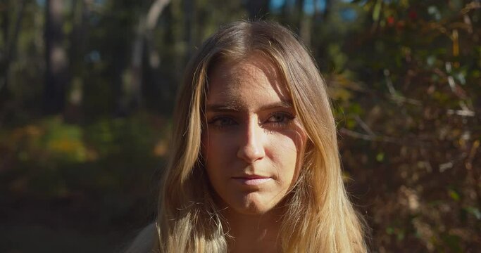 Portrait of Poker face blond woman turning around and looking into the camera at an outdoor wild forest