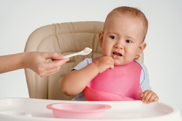 A baby in a pink bib refuses to eat with a spoon