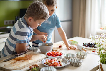 Funny brother male kids rejoicing having fun cooking summer dessert with fruits and berries