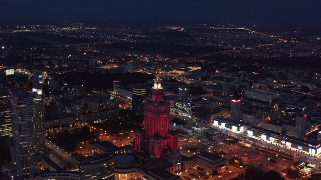 Aerial panoramic footage of large city at night. Palace of Culture and Science illuminated by red light. Warsaw, Poland