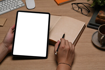 Young man holding digital tablet and making notes on notebook.