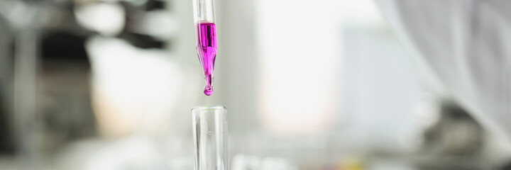 Scientist drops purple liquid from pipette into test tube
