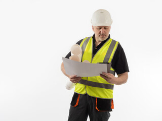 Fototapeta premium Civil engineer examines the documentation. Man builder holds a large poster in his hands and examines it. Builder in a yellow vest on a white background. Experienced engineer in a white helmet