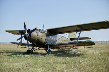 Fototapeta na wymiar An old Soviet AN 2 aircraft of protective color stands at the airfield in a green field