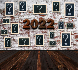 2022 Happy New Year seasonal background in large empty room with question marks - white chalk drawing on small blackboard hanging old brick wall and number