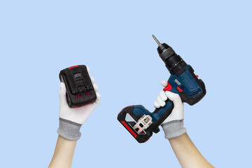 Gloved hands holding screwdriver, drill and battery construction tools. Work tools on blue background.
