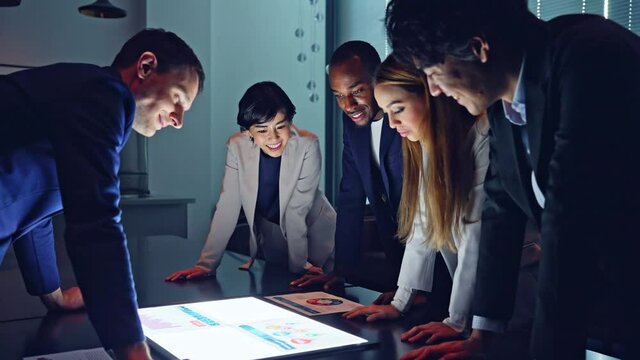 夜のオフィスで画面を見ながら会議する多国籍グループ　スローモーション 