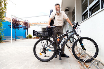 Obraz premium Mature caucasian man stands next to bicycle in a bike parking space. Copy space.