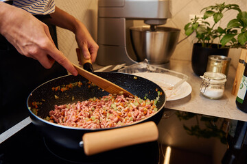 Woman cooking bolognese sauce in pan on induction stove in the kitchen