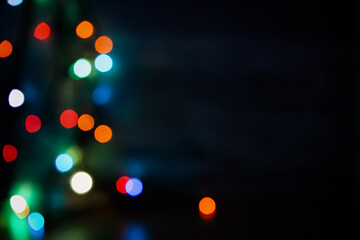 Multi-colored bokeh on a black background. Bright blurry textures of holiday lights. Colorful beautiful Christmas garlands on blurry background. Layout of a greeting card for the New year. Copy space