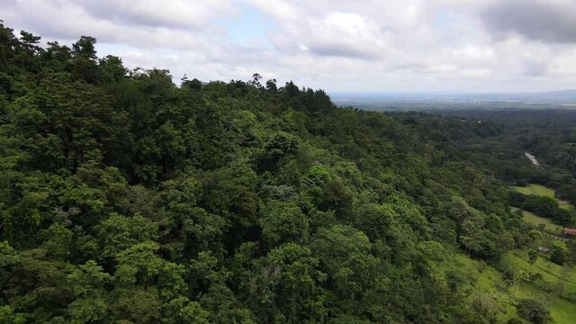 Drone flying and orbiting along side of a mountain covered by thick rainforest in central America. Cinematic aerial footage of Costa Rican landscapes and secluded lonely house on top of the hill.