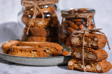 Traditional Italian cantuccini cookies with almonds in glass jar. Sweet dried biscuits. Homemade fresh Italian cookies cantuccini stacks and organic almond seeds. Healthy organic eating - obrazy, fototapety, plakaty
