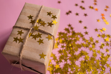 Gift in kraft packaging on a pink background with confetti in the form of stars. Holiday. Birthday. Christmas. March 8