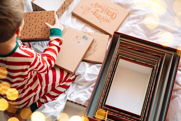 Child in striped pajamas standing next to open boxes on white bed