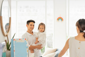 Fototapeta premium PAPÁ ORIENTAL CON SU HIJA EN BRAZOS DENTRO DE SU HOGAR HABLANDO CON SU ESPOSA