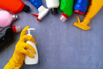 Cleaning supplies with hands in rubber gloves on gray background