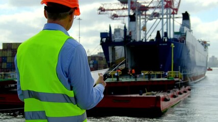 Ship cargo loading process. Customs officer in yellow vest makes report of new delivered freight looking at workers team near open ship hold in dock