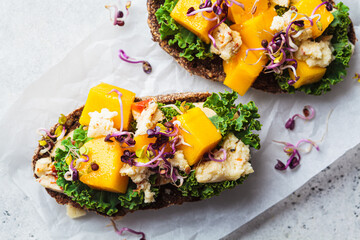 Rye toast with goat cheese, mango and kale, gray background. Healthy food concept.