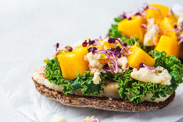 Rye toast with goat cheese, mango and kale, gray background. Healthy food concept.