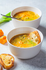 Homemade broccoli cheddar cheese soup with green onions in white bowl, gray background. Vegetarian food concept.