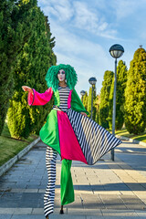 Female clown on stilts walking on paved path in green park