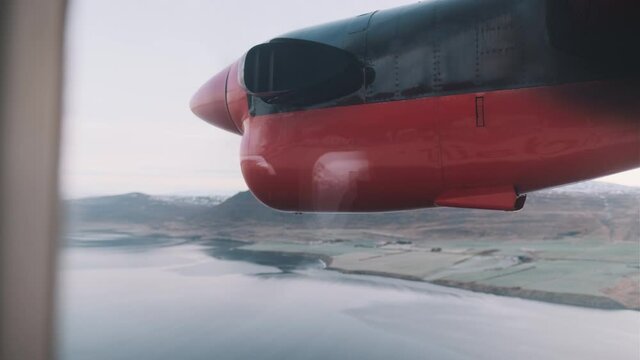 View out window of small plane propeller as plane flies over Iceland fjord. Handheld.