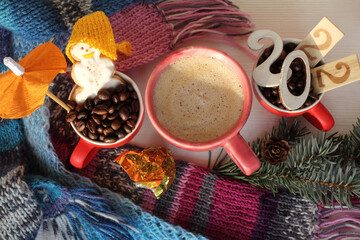 Obraz na płótnie Canvas cups with cappuccino, coffee beans, gingerbread snowman, knitted scarves, spruce branch on the table top view. merry warming frothy 2022