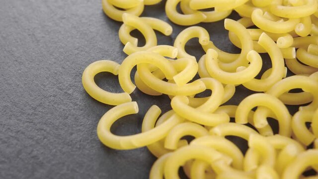 Dry Italian Gobbetti pasta on a stone black slate surface. Macro. Slow rotation. Uncooked wheat macaroni. Mediterranean cuisine