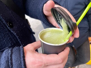 A man holding a paper cup with green matcha tea.