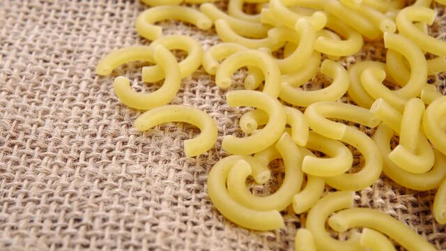 Dry yellow gobetti pasta on a rustic rough burlap. Carbohydrate wheat vegetarian food. Macro. Rotation