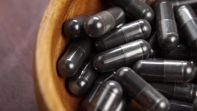 Charcoal black capsules fall into a wooden bowl in slow motion. Macro. Activated carbon. Natural absorbent