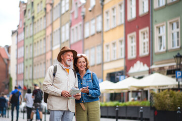 Portrait of happy senior couple tourists using map and smartphone outdoors in town street