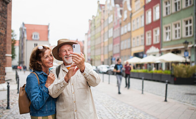 Portrait of happy senior couple tourists making selfie outdoors in historic town