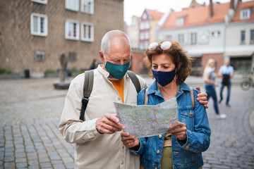 Senior couple tourists with face masks using map outdoors in town street