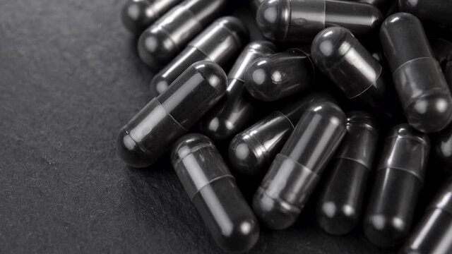 Charcoal black capsules on a slate stone. Macro. Slow rotation. Dramatic view. Carbon pills