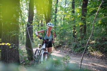 Active senior woman biker pushing ebike outdoors in forest.