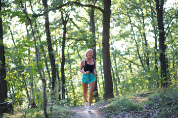 Happy active senior woman jogging outdoors in forest.