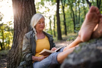 Poster Senior woman relaxing and reading book outdoors in forest. © Halfpoint