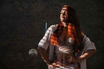 A redhead, young girl in beautiful underwear stands in the bathroom in the rays of light through the blinds