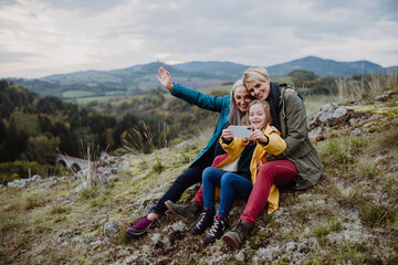 Small girl with mother and grandmother taking selfie outoors on top of mountain.