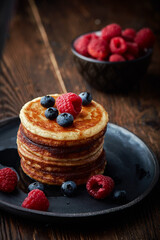 Tasty appetizing homemade pancakes served with honey and raspberries on plate on dark background