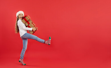 Christmas ads banner. Adorable cheerful teen girl steps with Christmas presents isolated on red...