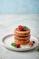 Tasty appetizing homemade pancakes served with honey, raspberries and blueberries on plate on grey background